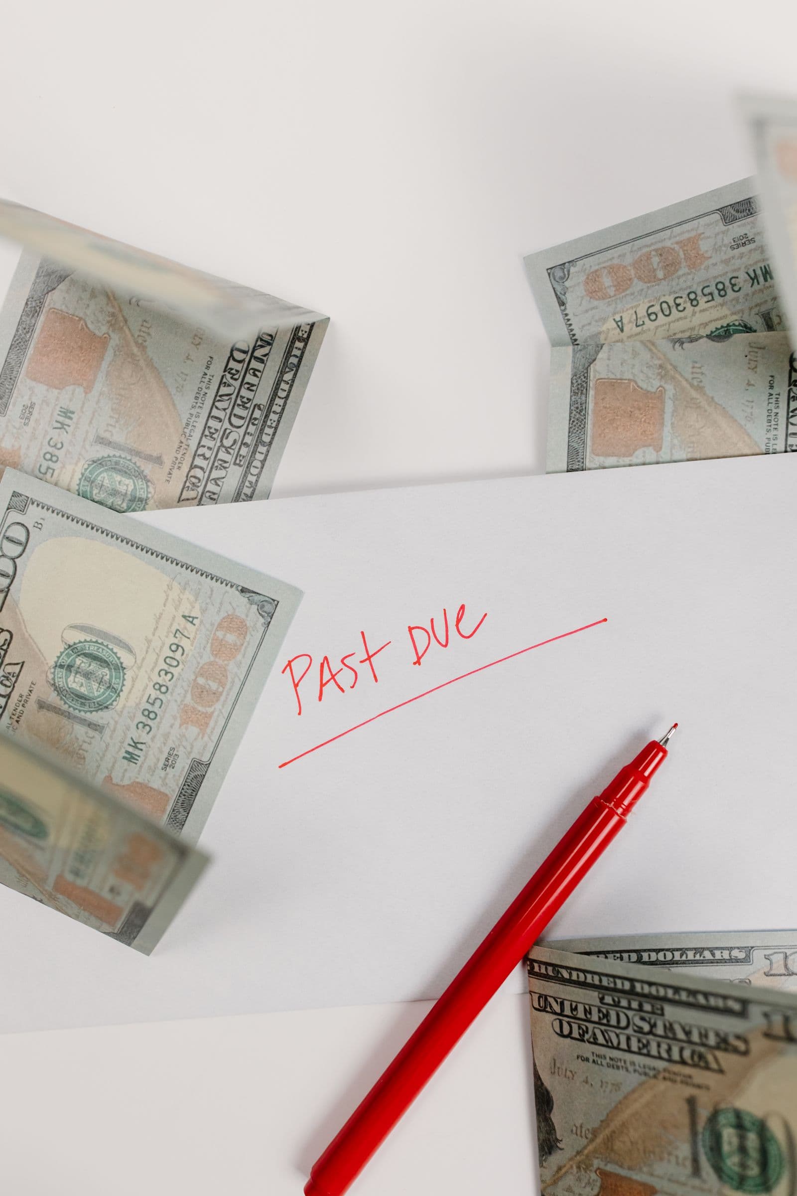 An envelope marked past due beside dollar bills and a red pen