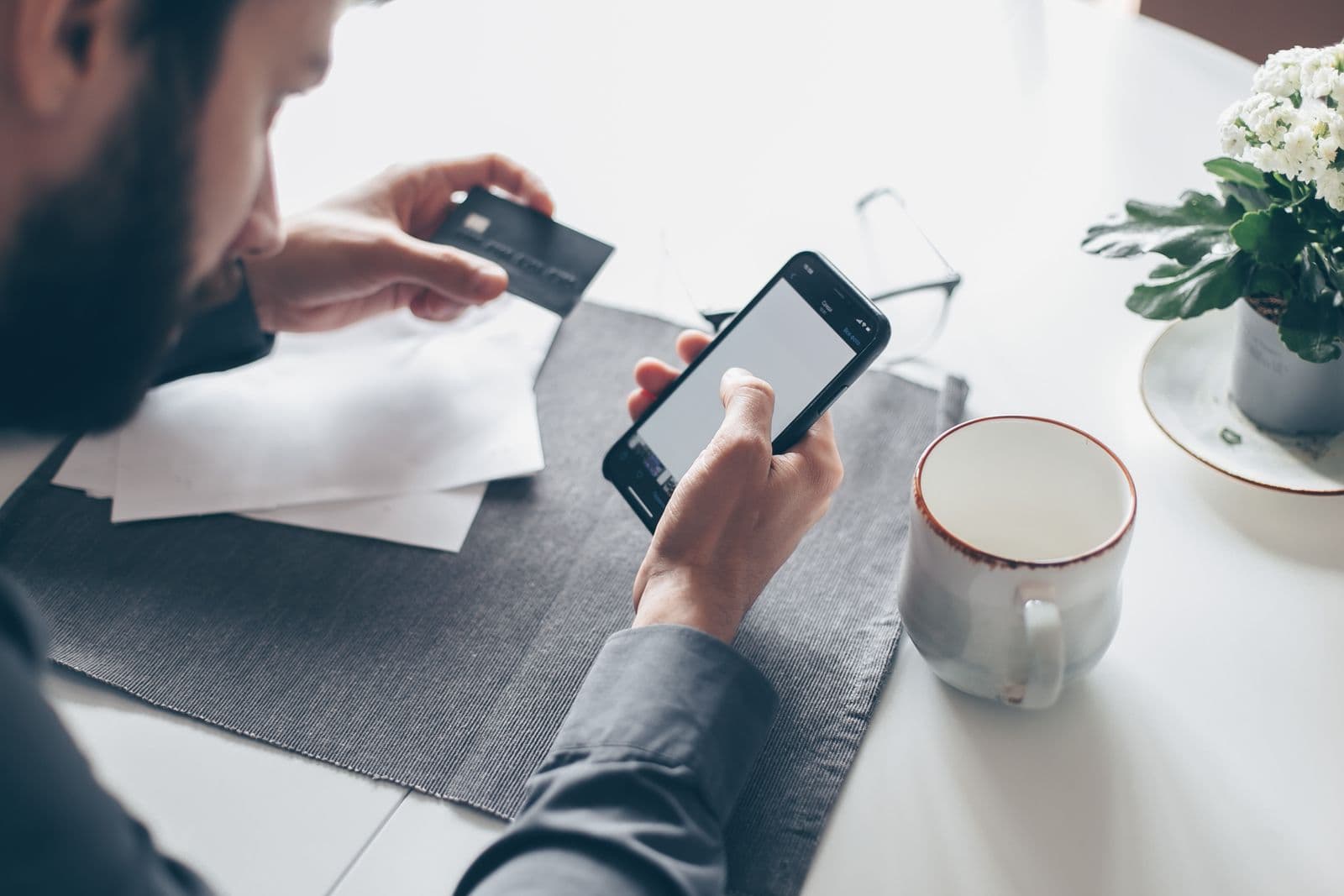 Hands holding a credit card and a phone to pay a bill at a desk