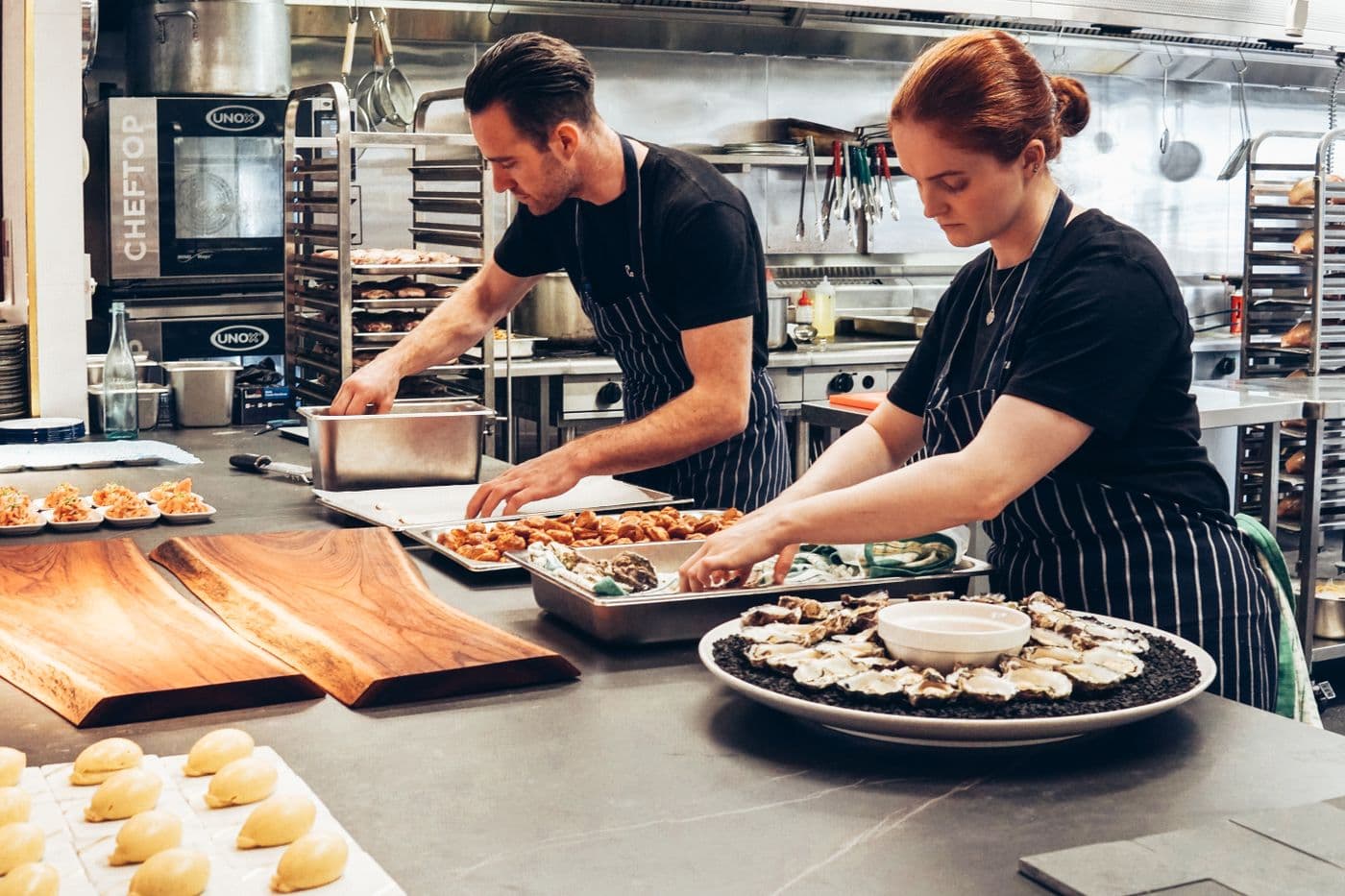 Two chefs with their hands full preparing dishes in a busy kitchen