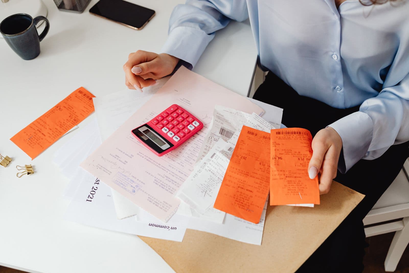 Hands sorting receipts next to a calculator on a desk