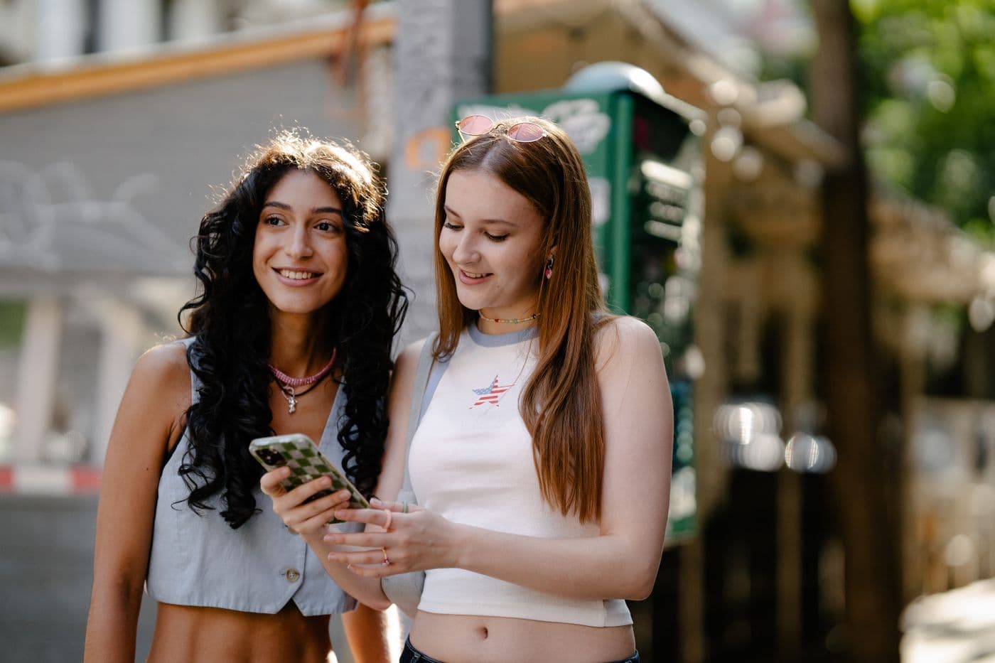 Two young women looking at a phone on a city street