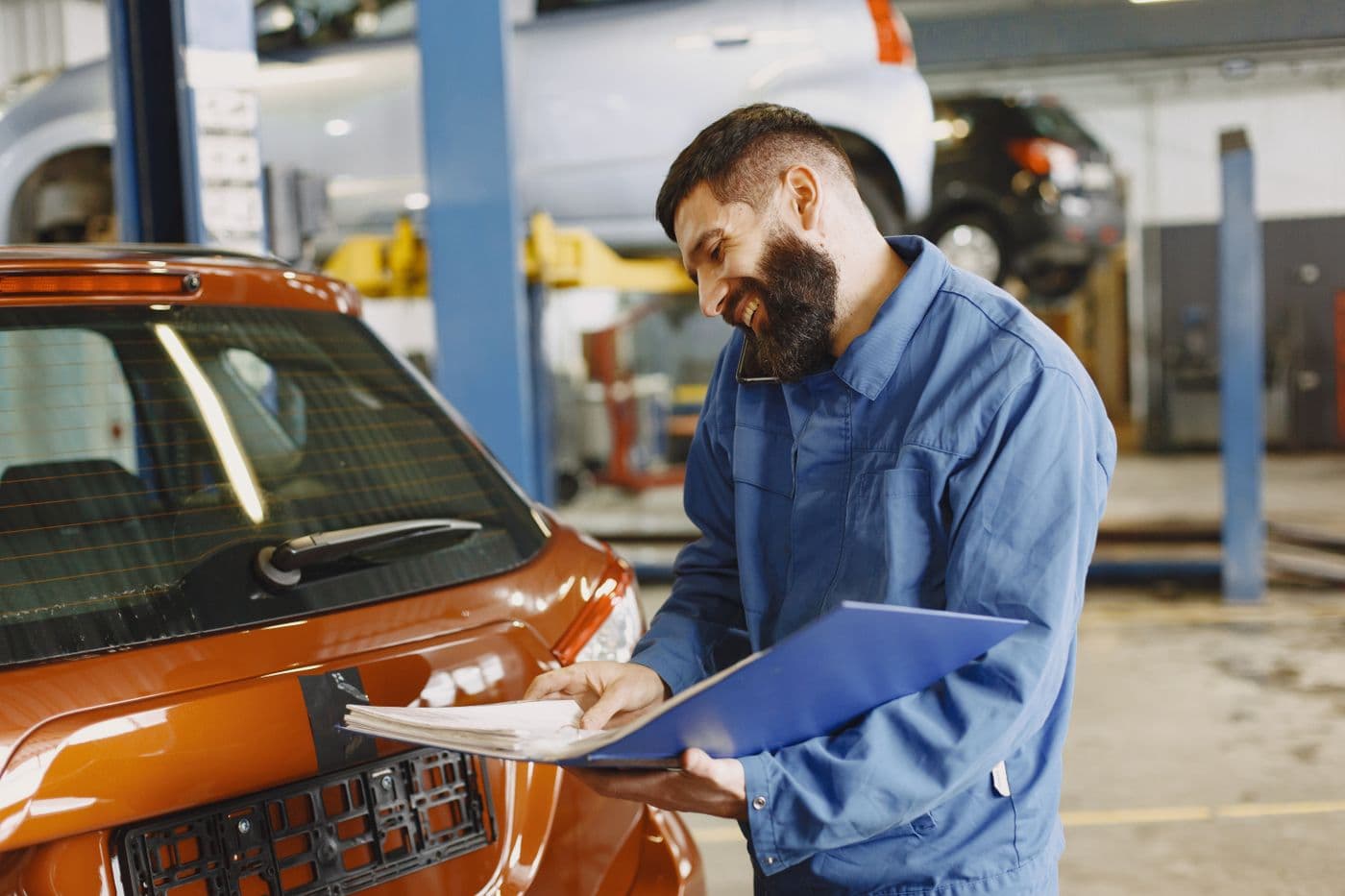 A mechanic with a clipboard inspecting a car in a service garage