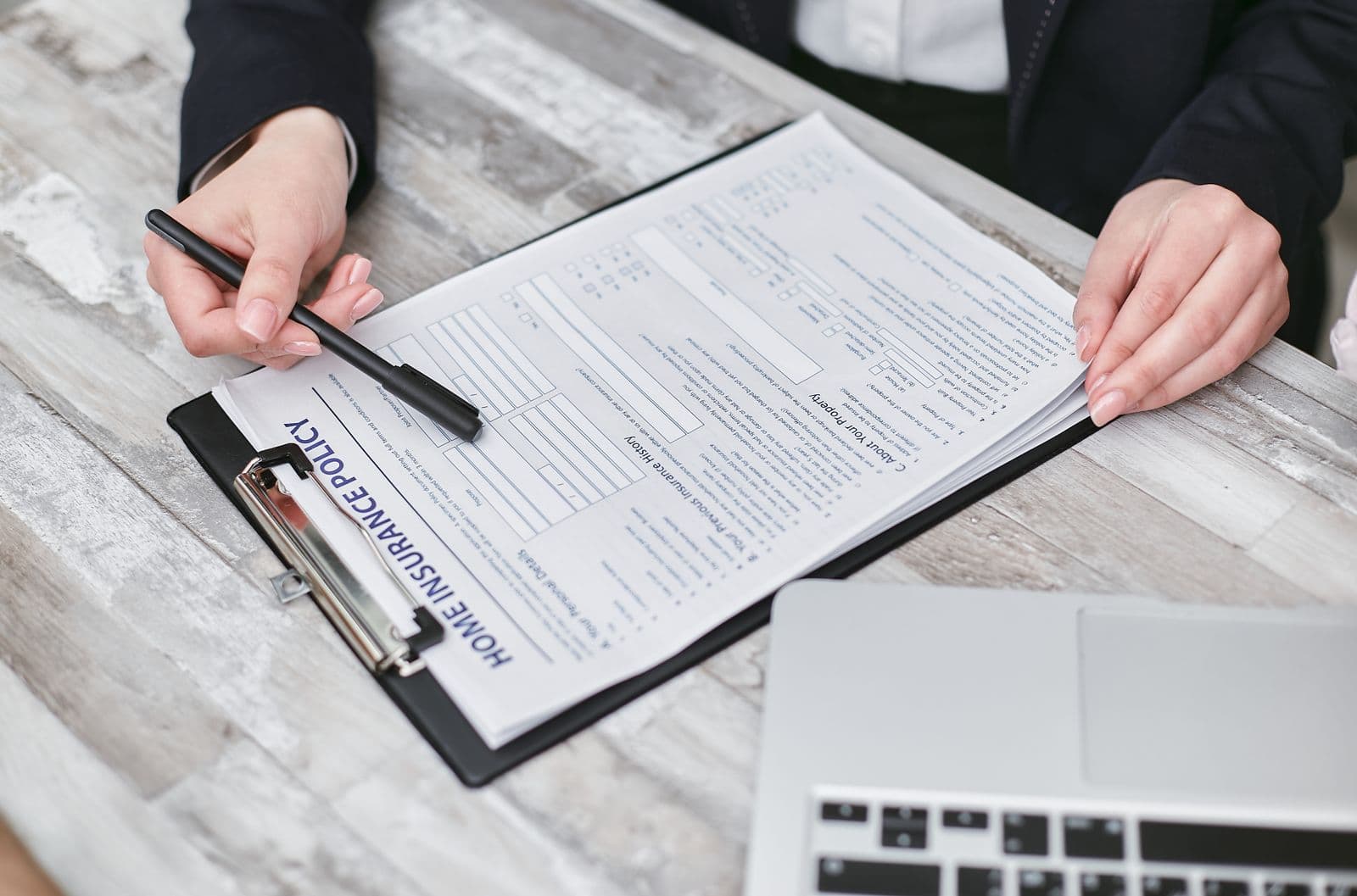 Hands reviewing a home insurance policy form on a clipboard beside a laptop