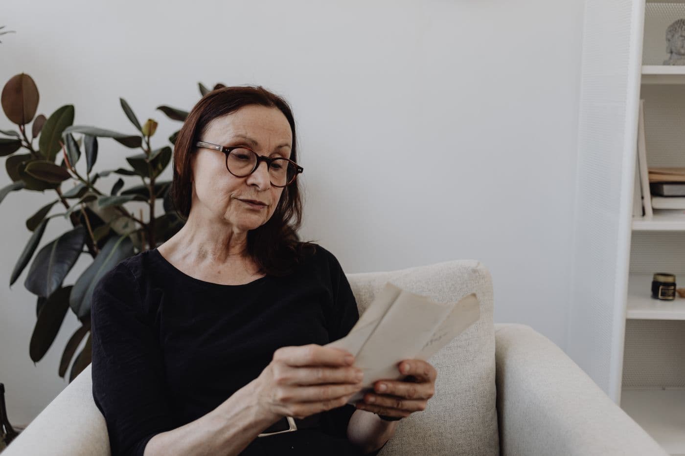 An older woman in an armchair reading letters